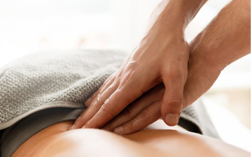 Nahaufnahme: Therapeut übt gezielten Druck auf den Rücken einer Person aus (Faszienbehandlung), teilweise mit Handtuch bedeckt.