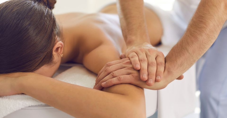 Therapeut führt eine manuelle Behandlung am Arm einer Patientin auf der Therapieliege durch (Drucktechnik/Mobilisation).