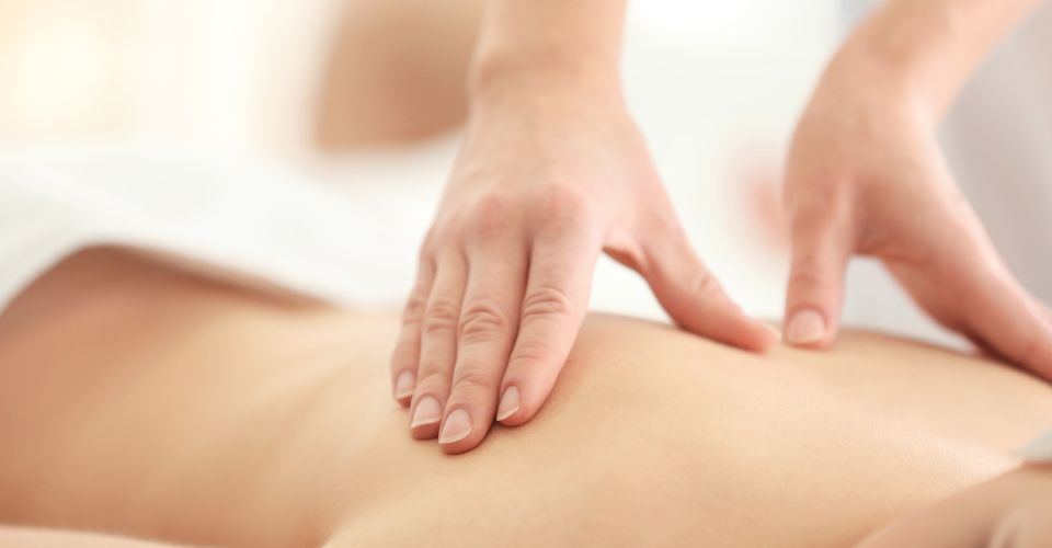 Nahaufnahme: Hände einer Therapeutin behandeln den Rücken einer liegenden Person mit sanftem Druck (manuelle Therapie/Massage).