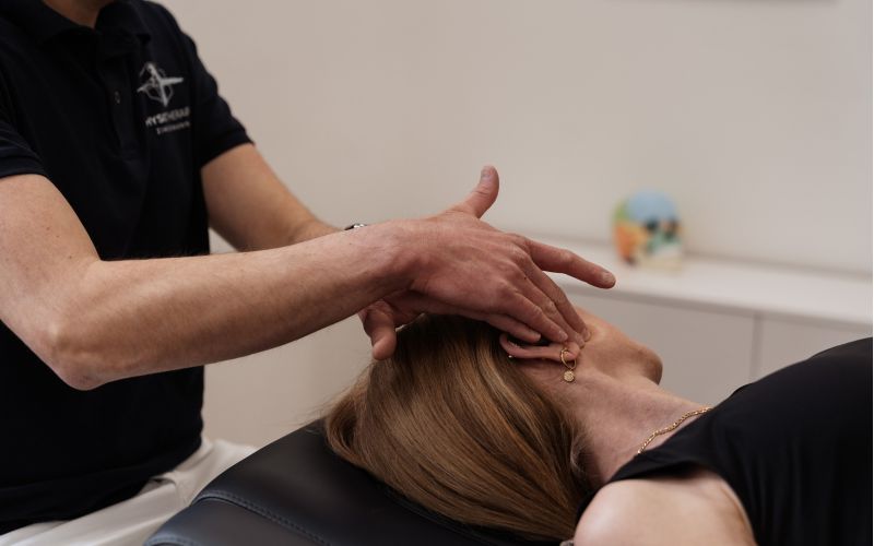 Physiotherapeut behandelt eine Patientin auf der Liege mit sanften Handgriffen im Kopf- und Kieferbereich (manuelle Therapie/Osteopathie).