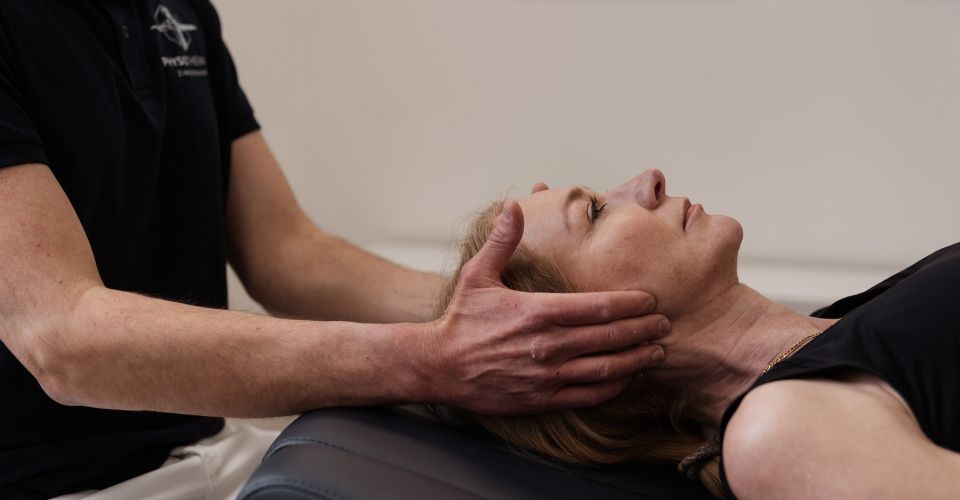 Physiotherapeut führt sanfte manuelle Behandlung im Nacken- und Kopfbereich einer Patientin durch, die entspannt auf der Therapieliege liegt.