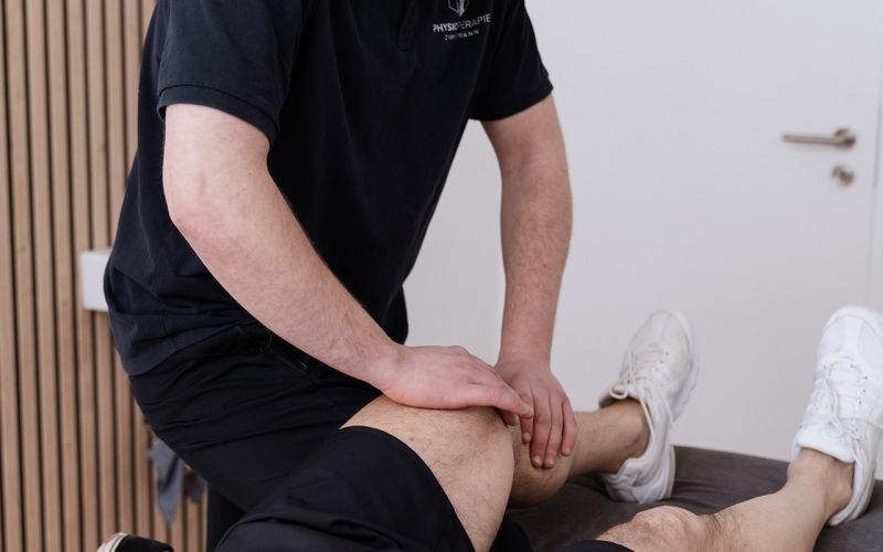Ein Patient wird auf Behanldungsbank am Knie massiert